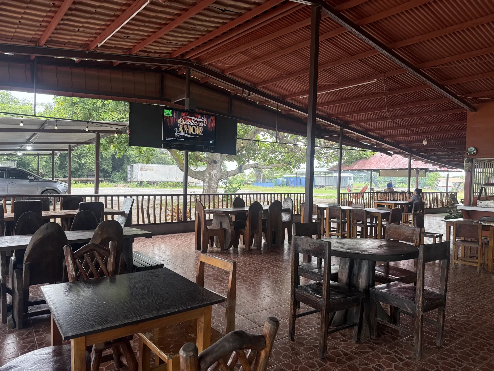 Mesas redondas de madera oscura en el comedor, con televisor y patio trasero