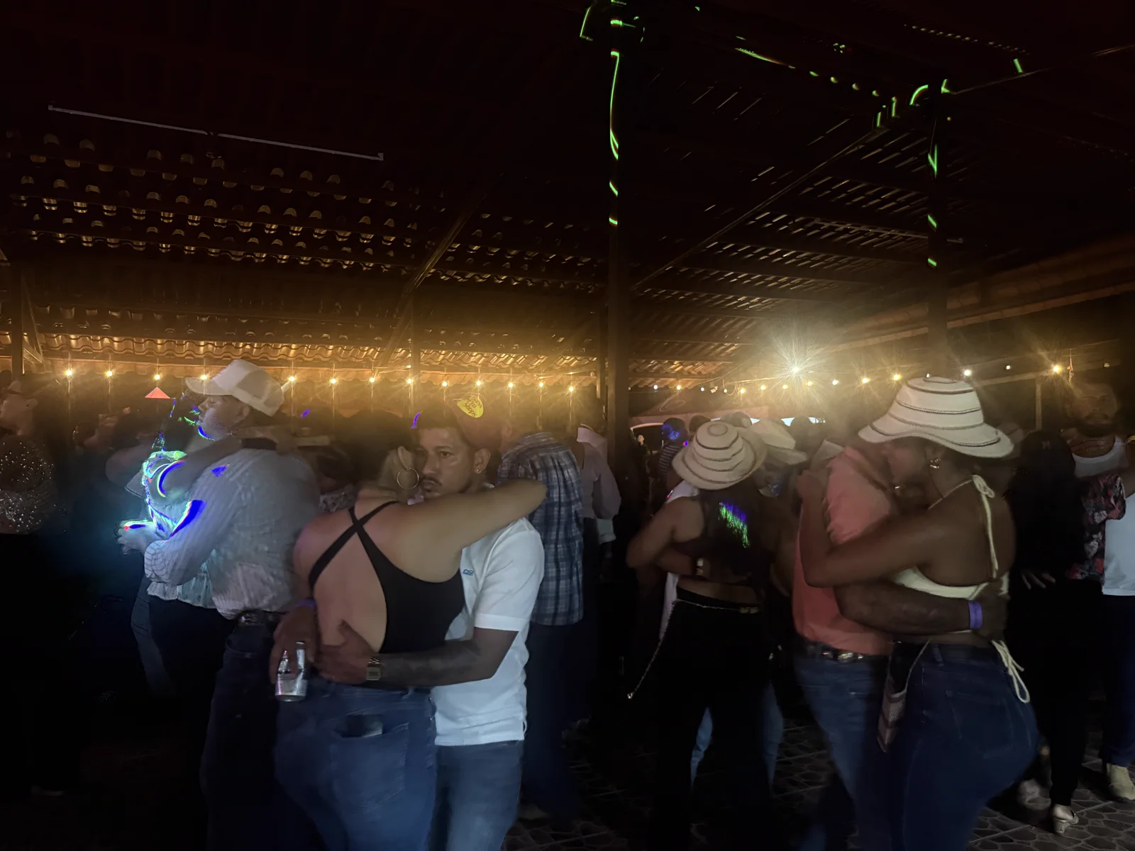 Parejas bailando muy cerca bajo las luces colgantes del rancho, en una noche especial de música en vivo