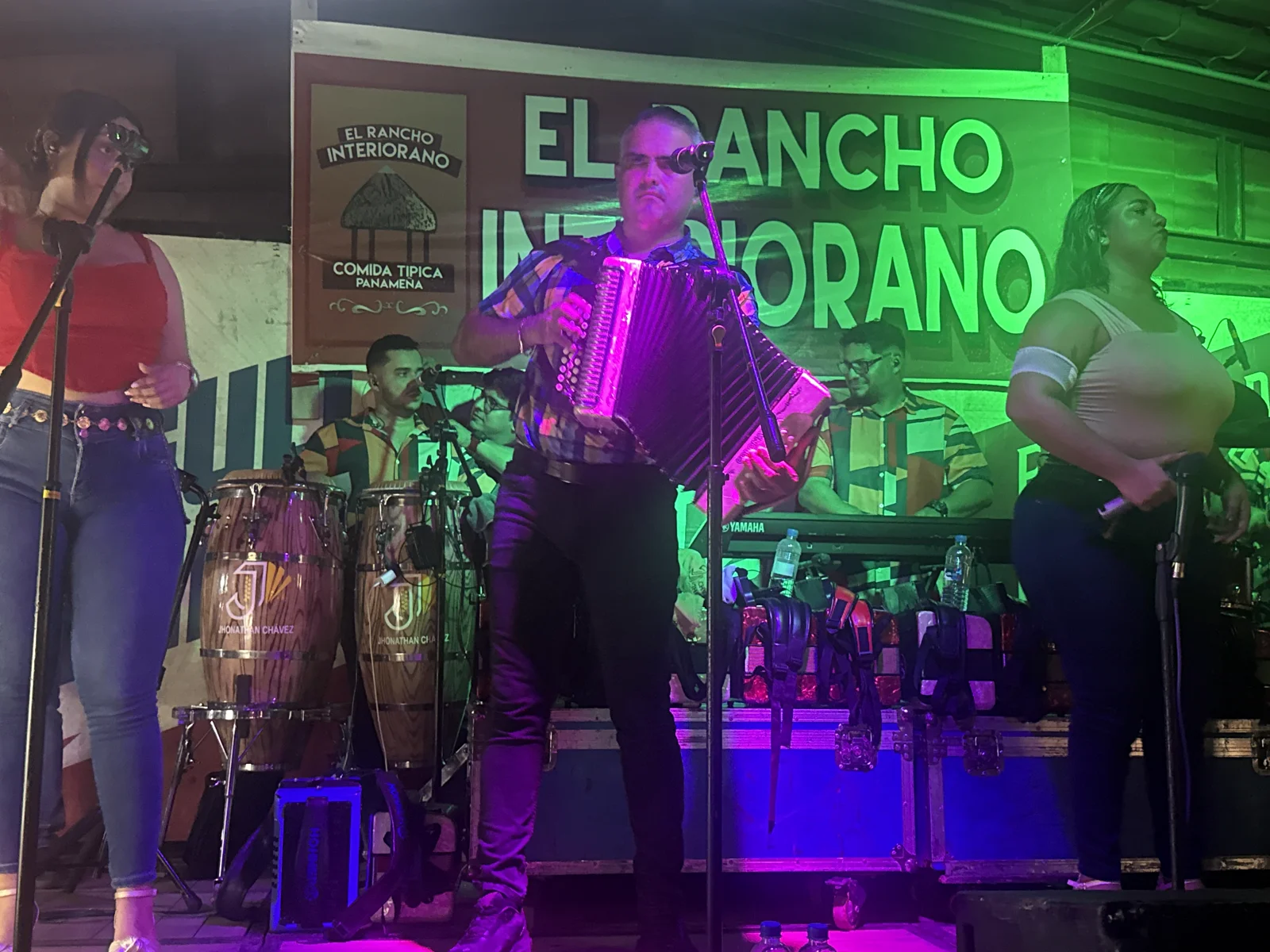 El acordeonista de la orquesta cantando frente al banner de El Rancho Interiorano, con las congas de la tarima al fondo