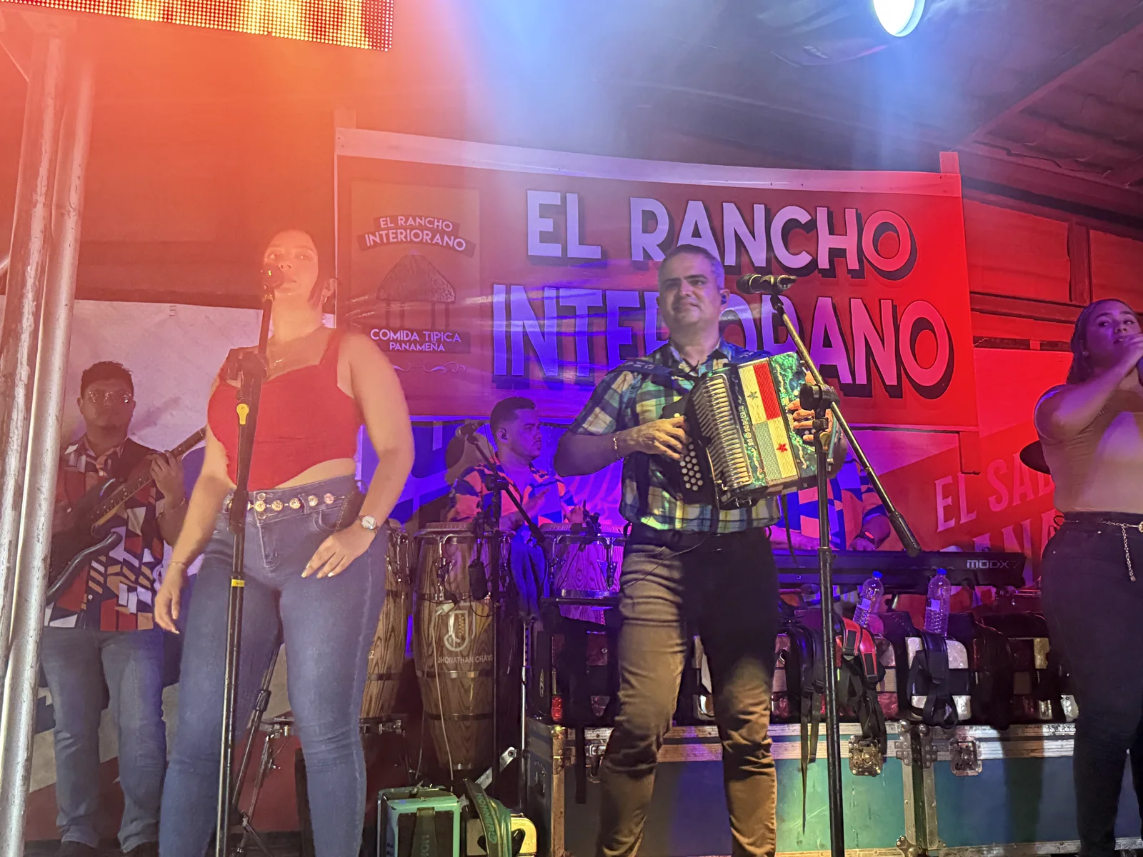 La orquesta completa tocando en la tarima frente al banner grande de El Rancho Interiorano, con luces de escenario
