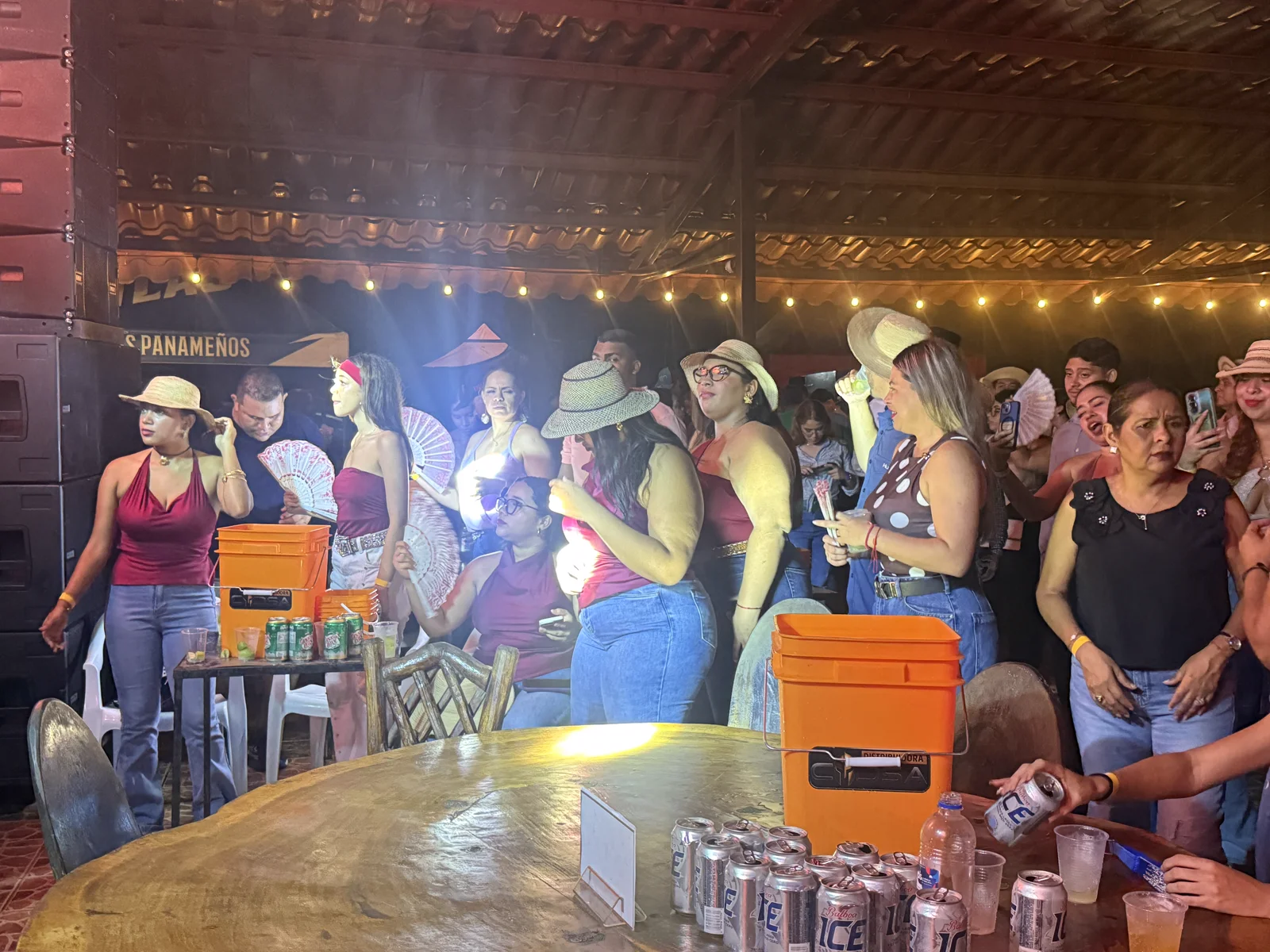Grupo de mujeres con sombreros y abanicos junto a una cava de cervezas, durante una noche especial en el rancho
